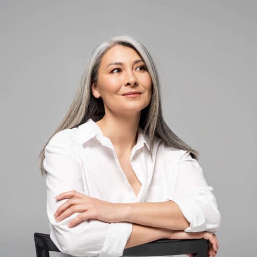 beautiful dreamy asian woman with grey hair sitting on chair isolated on grey