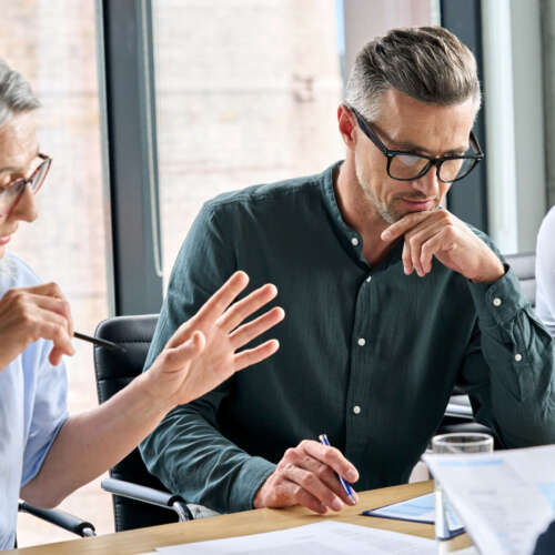 Serious mature caucasian male ceo executive manager with male business partner discussing corporation merge plan at board room table. Professional coworkers leaders doing paperwork in modern office.
